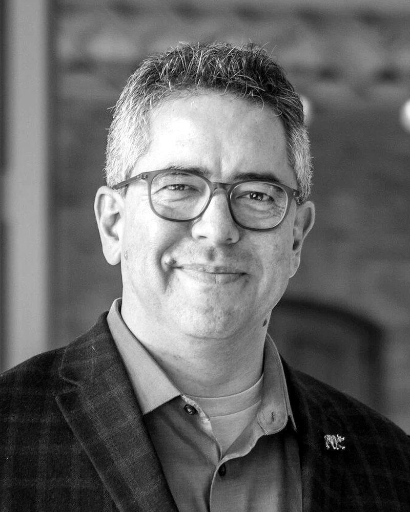 Black-and-white portrait of Fernando Pérez, wearing glasses and a jacket, smiling at the camera.